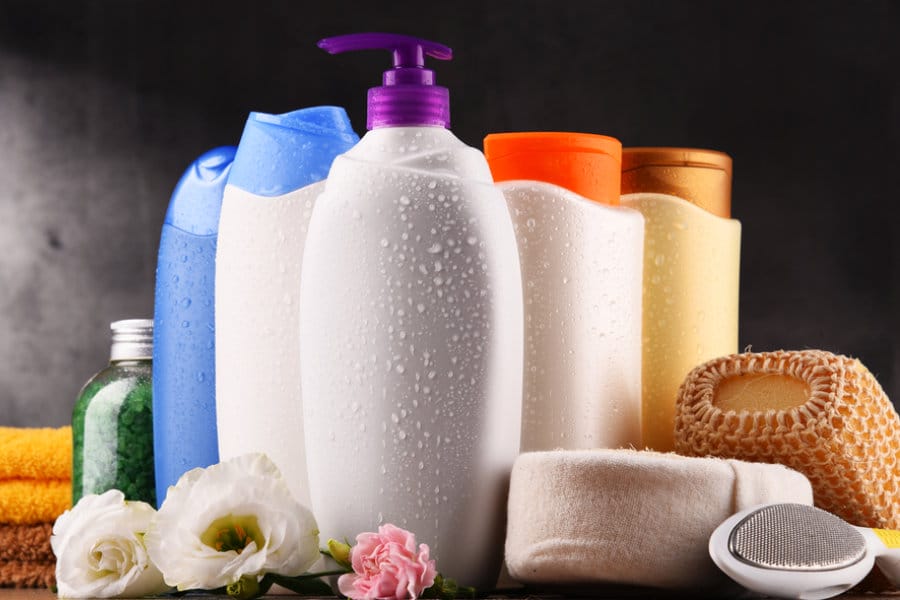 Una selección de botellas de champú y loción, elegantemente dispuestas con una toallita, una piedra pómez y flores sobre una superficie. Descubra el toque de lujo con nuestra exclusiva colección Marcas Privadas.